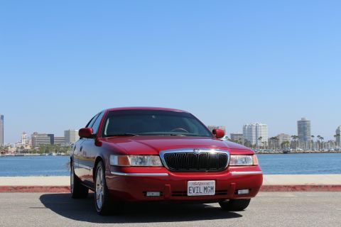 2002 Mercury Grand Marquis - A red 2002 Mercury Grand Marquis is parked in front of a city skyline and harbor.