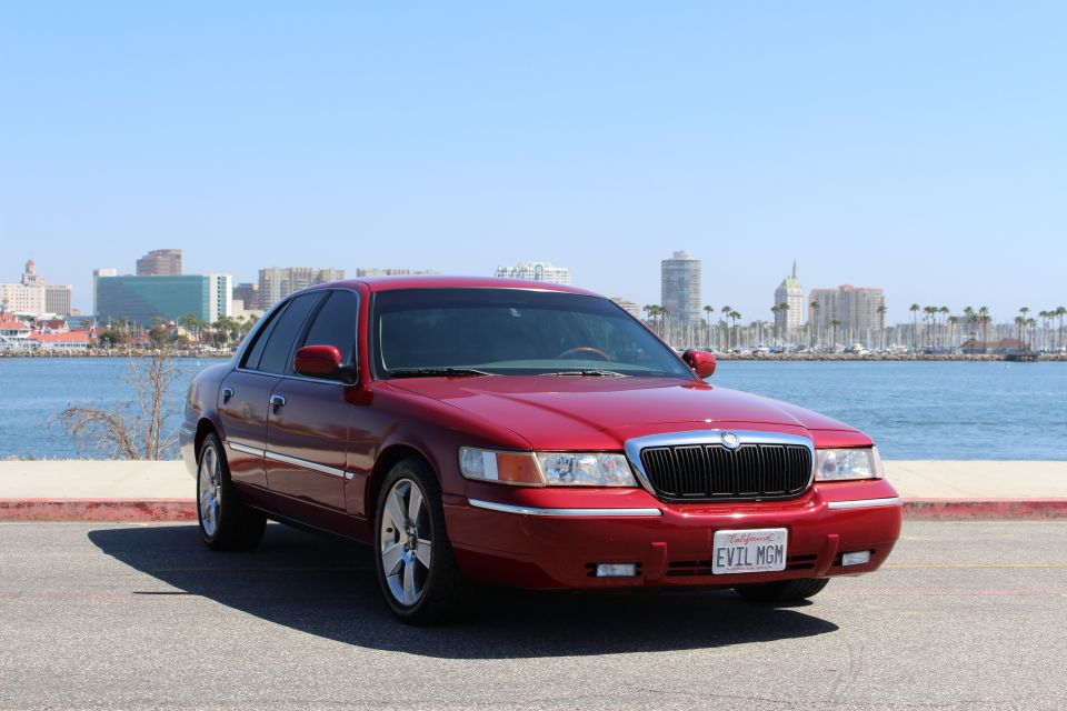 Red sedan parked by the water with city buildings in the background. License plate says EVIL MGM