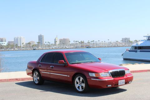 2002 Mercury Grand Marquis - 2002 Mercury Grand Marquis parked near a harbor with a city skyline and a large yacht visible.