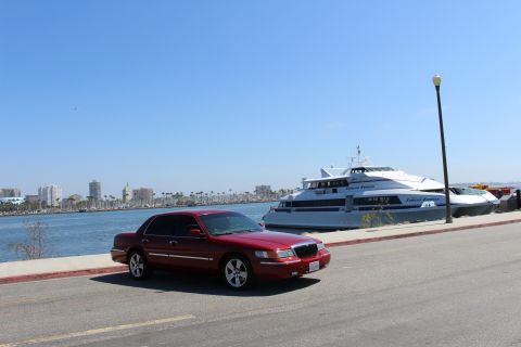 2002 Mercury Grand Marquis - A red 2002 Mercury Grand Marquis is parked by the water with a large ferry and city skyline in the background.