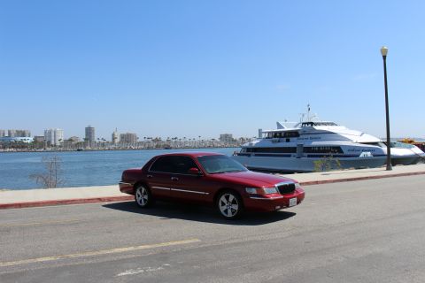 2002 Mercury Grand Marquis - A red 2002 Mercury Grand Marquis is parked near a harbor with a modern ferry and city skyline.