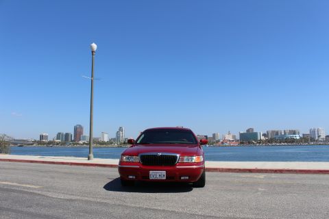2002 Mercury Grand Marquis - A red 2002 Mercury Grand Marquis is parked facing the camera with a city skyline in the background.