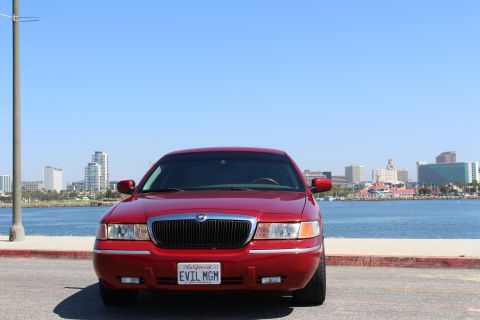 2002 Mercury Grand Marquis - Front view of a red 2002 Mercury Grand Marquis parked by the water with a city skyline in the background.