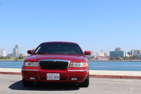 2002 Mercury Grand Marquis - Front view of a red 2002 Mercury Grand Marquis with a city skyline and water behind it.