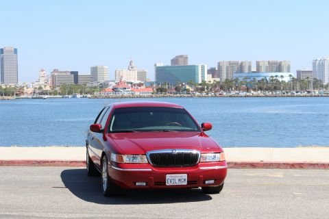 2002 Mercury Grand Marquis - A red 2002 Mercury Grand Marquis is parked by the water with a city skyline behind it.