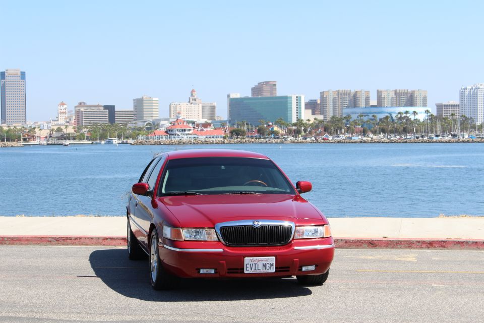 Red 2002 Mercury Grand Marquis parked by the water with city skyline in background