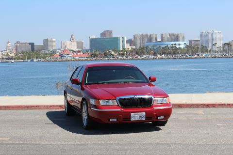 2002 Mercury Grand Marquis - A red 2002 Mercury Grand Marquis is parked in front of a waterfront cityscape.