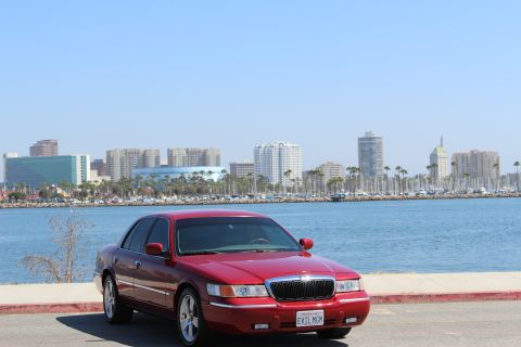 2002 Mercury Grand Marquis - A red 2002 Mercury Grand Marquis is parked near a waterfront with a city skyline.