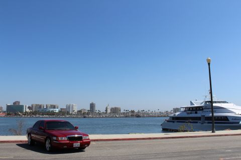 2002 Mercury Grand Marquis - A red 2002 Mercury Grand Marquis is parked near a waterfront with a city skyline and a large passenger boat.