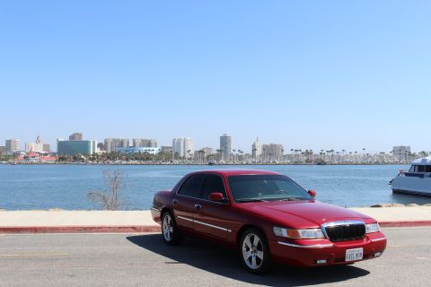 2002 Mercury Grand Marquis - A red 2002 Mercury Grand Marquis is parked near a waterfront with a city skyline visible across the water.