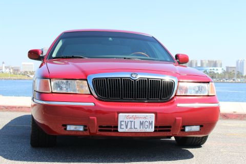 2002 Mercury Grand Marquis - A red 2002 Mercury Grand Marquis is parked facing the camera with a waterfront city skyline in the background.