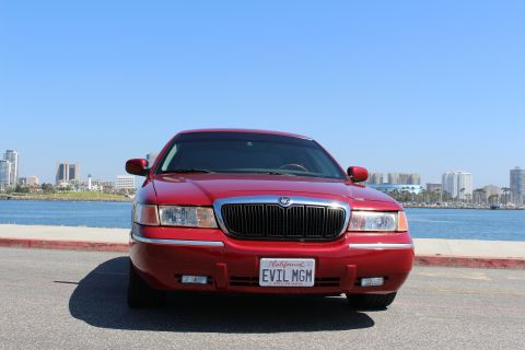 2002 Mercury Grand Marquis - A red 2002 Mercury Grand Marquis is parked near a waterfront with a city skyline in the distance.