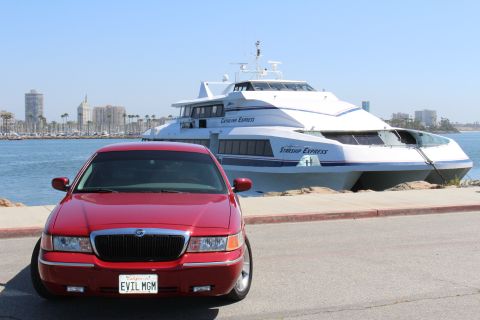 2002 Mercury Grand Marquis - A red 2002 Mercury Grand Marquis is parked in front of a large passenger ferry with a city skyline in the background.