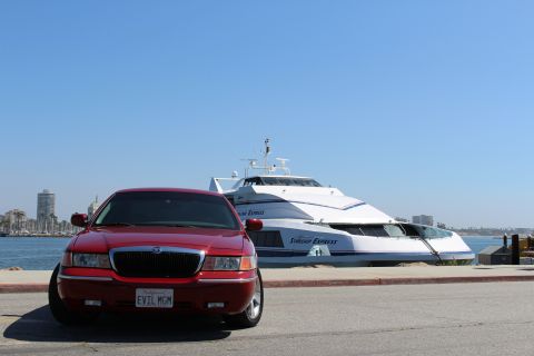2002 Mercury Grand Marquis - A red 2002 Mercury Grand Marquis is parked next to the Starship Express yacht with a city skyline in the background.