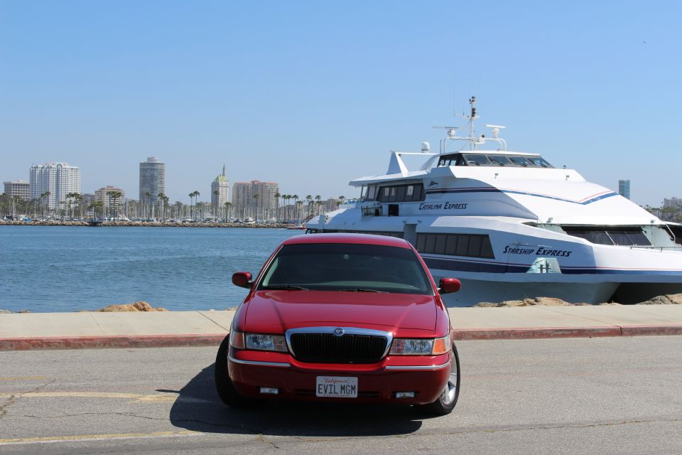Red 2002 Mercury Grand Marquis parked by the water with a ferry and city skyline in the background