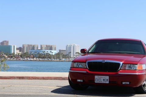 2002 Mercury Grand Marquis - A red 2002 Mercury Grand Marquis is parked near a body of water with a city skyline in the background.