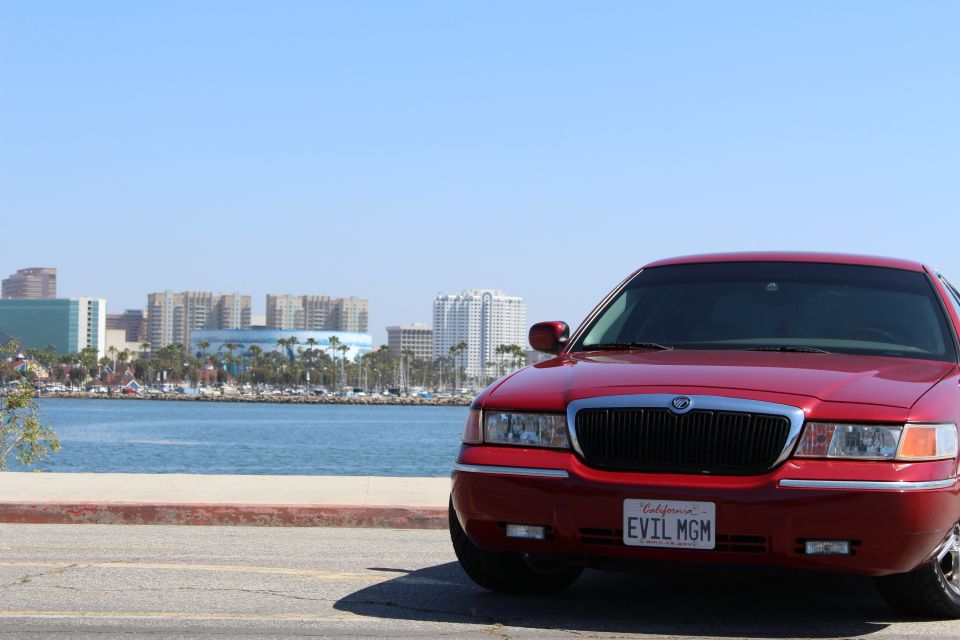 Red 2002 Mercury Grand Marquis parked by the water with a city skyline