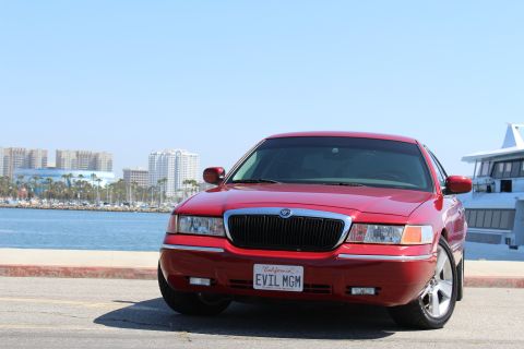 2002 Mercury Grand Marquis - Front view of a red 2002 Mercury Grand Marquis parked near a harbor with city buildings in the background.