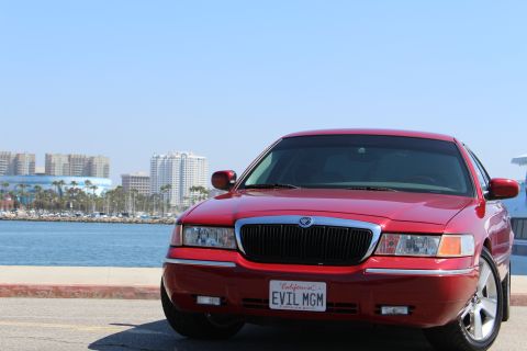 2002 Mercury Grand Marquis - A red 2002 Mercury Grand Marquis is parked near a body of water with buildings in the distance.