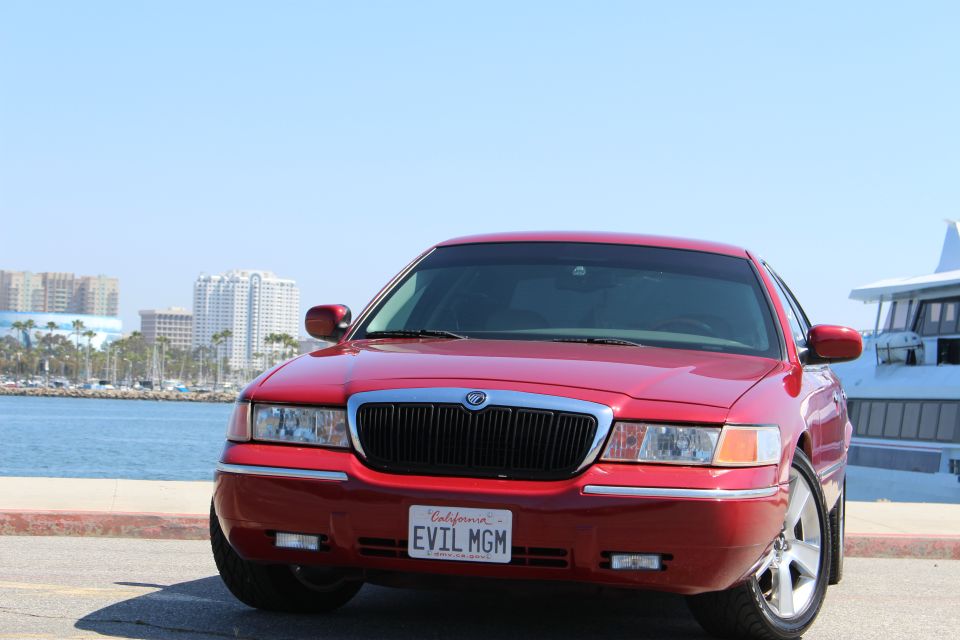 Red 2002 Mercury Grand Marquis with custom 'EVIL MGM' license plate, front view, parked by a waterfront