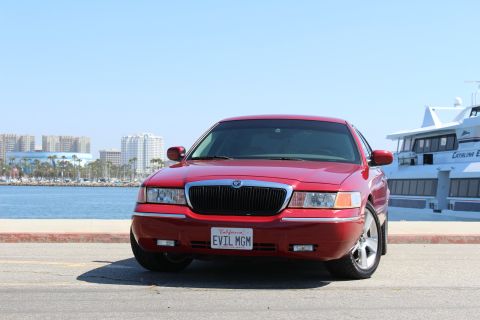 2002 Mercury Grand Marquis - Front view of a red 2002 Mercury Grand Marquis parked by the water with a boat and city skyline.