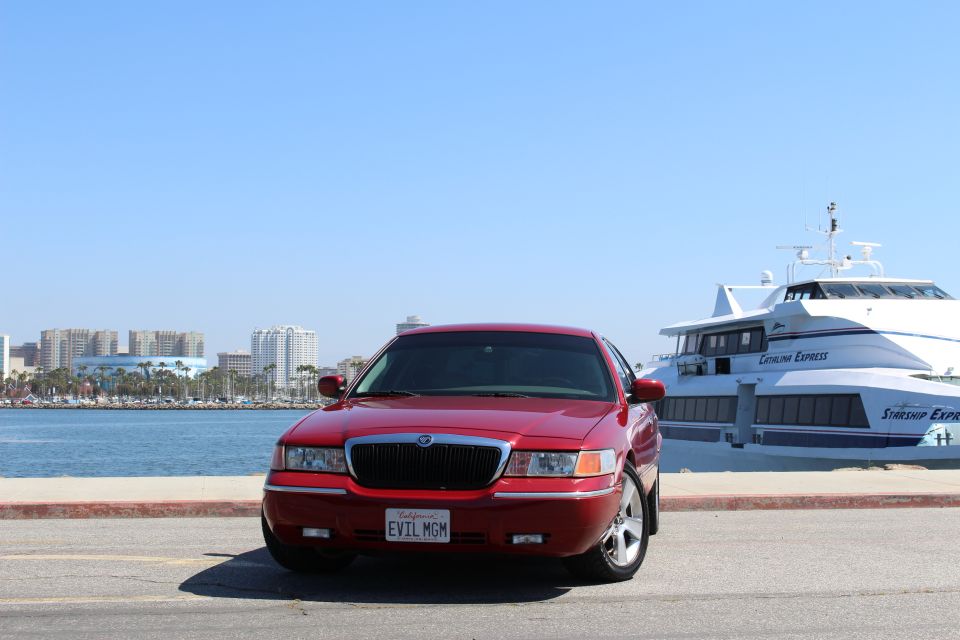 Red 2002 Mercury Grand Marquis parked by a large white boat and city skyline