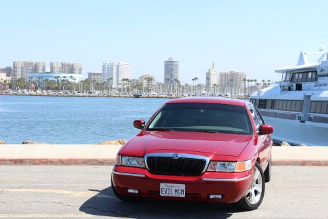 2002 Mercury Grand Marquis - Red 2002 Mercury Grand Marquis parked by the water with a cityscape and yacht in the background.