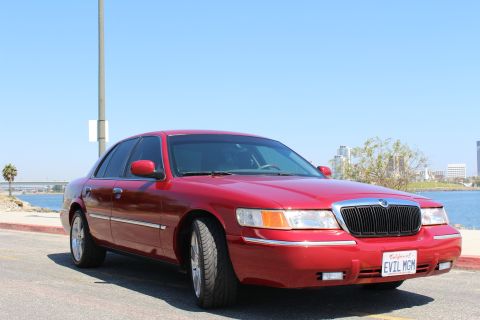 2002 Mercury Grand Marquis - A red Mercury Grand Marquis is parked near a body of water with a city skyline in the background.