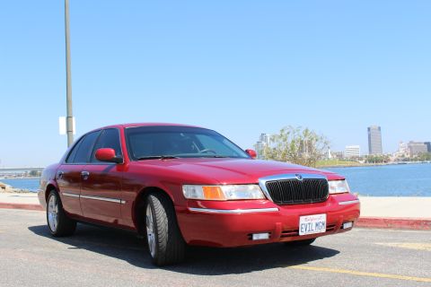 2002 Mercury Grand Marquis - A red 2002 Mercury Grand Marquis is parked by the water with a city skyline in the background.