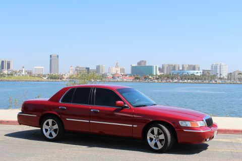 2002 Mercury Grand Marquis - A red 2002 Mercury Grand Marquis sedan is parked with a waterfront city view.
