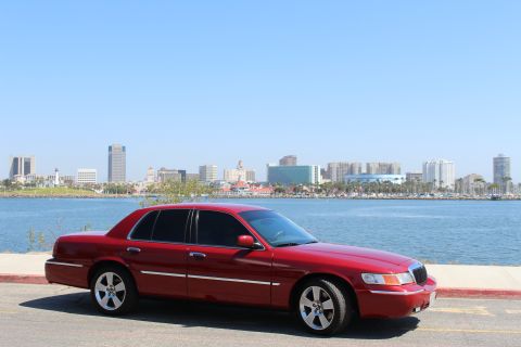 2002 Mercury Grand Marquis - A red 2002 Mercury Grand Marquis is parked near a waterfront with a city skyline visible across the water.