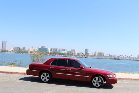2002 Mercury Grand Marquis - A red 2002 Mercury Grand Marquis is parked by the water with a city skyline in the distance.