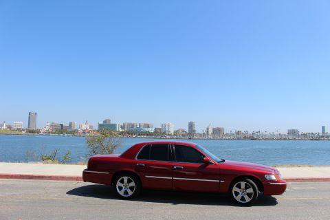 2002 Mercury Grand Marquis - A red 2002 Mercury Grand Marquis sedan is parked by the water with a city skyline in the background.