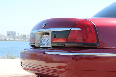 2002 Mercury Grand Marquis - Rear view of a red 2002 Mercury Grand Marquis, a custom license plate and a waterfront cityscape in the background.