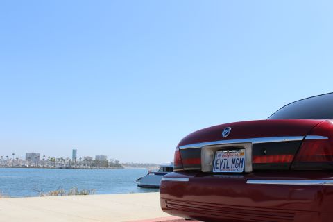 2002 Mercury Grand Marquis - A red 2002 Mercury Grand Marquis is seen from the rear at a waterfront location with a city skyline in the distance.