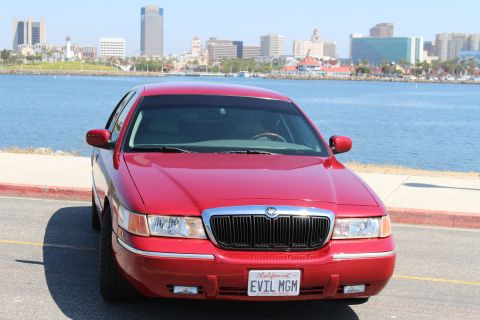 2002 Mercury Grand Marquis - A red 2002 Mercury Grand Marquis is parked by the water with a city skyline in the background.