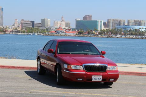 2002 Mercury Grand Marquis - Red 2002 Mercury Grand Marquis parked near a harbor with a city skyline in the distance.