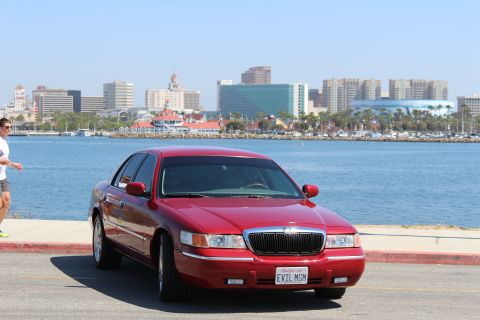 2002 Mercury Grand Marquis - A red 2002 Mercury Grand Marquis is parked by the water with a city skyline in the distance.