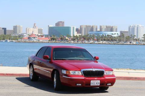 2002 Mercury Grand Marquis - A red 2002 Mercury Grand Marquis is parked near a waterfront with a city skyline.