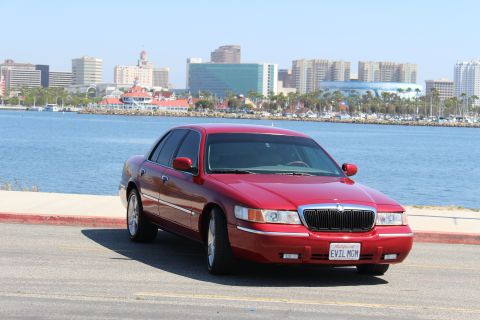 2002 Mercury Grand Marquis - A red 2002 Mercury Grand Marquis is parked near a body of water with a city skyline visible.