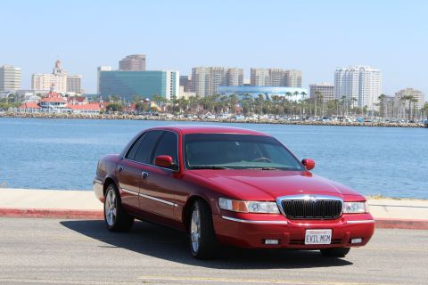 2002 Mercury Grand Marquis - A red 2002 Mercury Grand Marquis is parked with a city skyline and harbor in the background.