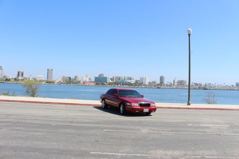 2002 Mercury Grand Marquis - A red 2002 Mercury Grand Marquis is parked by the water with a city skyline in the distance.