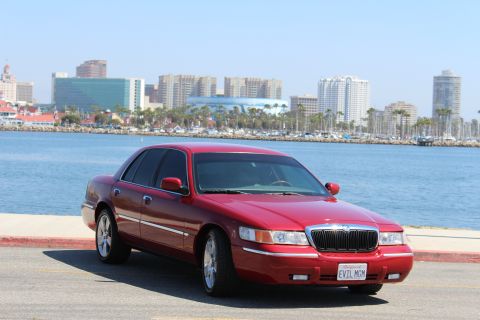 2002 Mercury Grand Marquis - A red 2002 Mercury Grand Marquis is parked near a waterfront with a city skyline.
