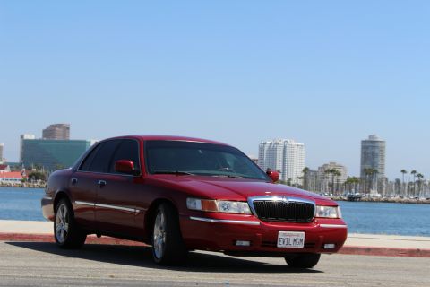 2002 Mercury Grand Marquis - A red 2002 Mercury Grand Marquis is parked near a waterfront with city buildings in the background.