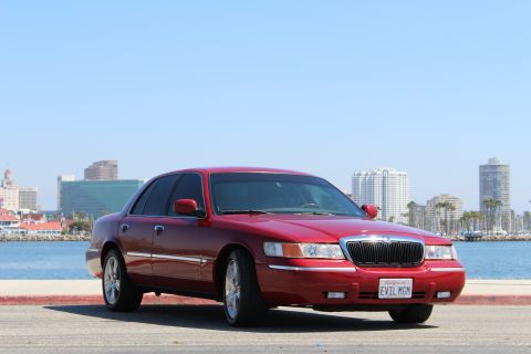 2002 Mercury Grand Marquis - A red 2002 Mercury Grand Marquis is parked near a waterfront with a city skyline.
