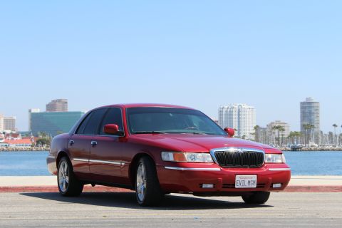2002 Mercury Grand Marquis - Red 2002 Mercury Grand Marquis parked near a waterfront with a city skyline behind it.