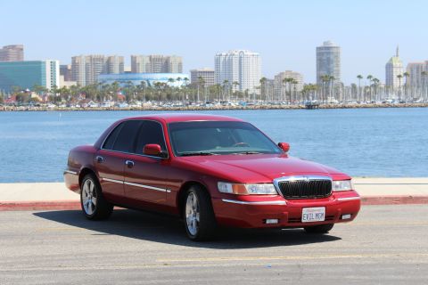 2002 Mercury Grand Marquis - A red 2002 Mercury Grand Marquis is parked near a waterfront with a city skyline.