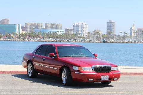 2002 Mercury Grand Marquis - A red 2002 Mercury Grand Marquis is parked near a waterfront with a city skyline.