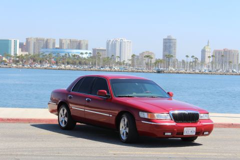2002 Mercury Grand Marquis - A red 2002 Mercury Grand Marquis is parked near a waterfront with a city skyline.