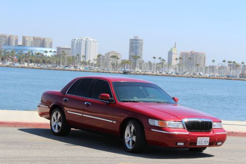 2002 Mercury Grand Marquis - A red 2002 Mercury Grand Marquis is parked near the water with a city skyline in the background.
